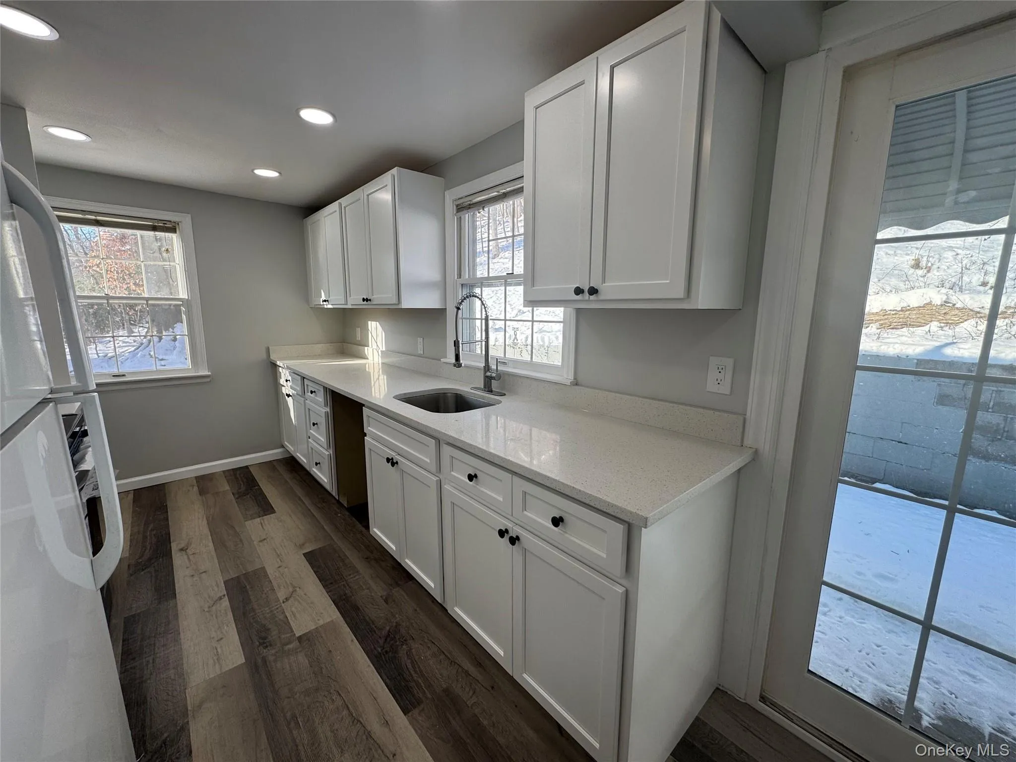 Kitchen with white cabinets, freestanding refrigerator, light stone countertops, dark wood-style flooring, and healthy amount of natural light Kitchen with white cabinets, freestanding refrigerator, light stone countertops, dark wood-style flooring, and healthy amount of natural light