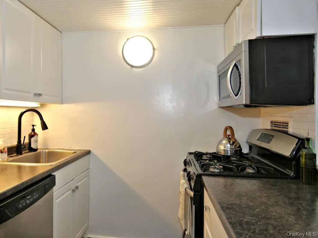 Kitchen featuring decorative backsplash, appliances with stainless steel finishes, white cabinetry, dark countertops, and wood ceiling Kitchen featuring decorative backsplash, appliances with stainless steel finishes, white cabinetry, dark countertops, and wood ceiling