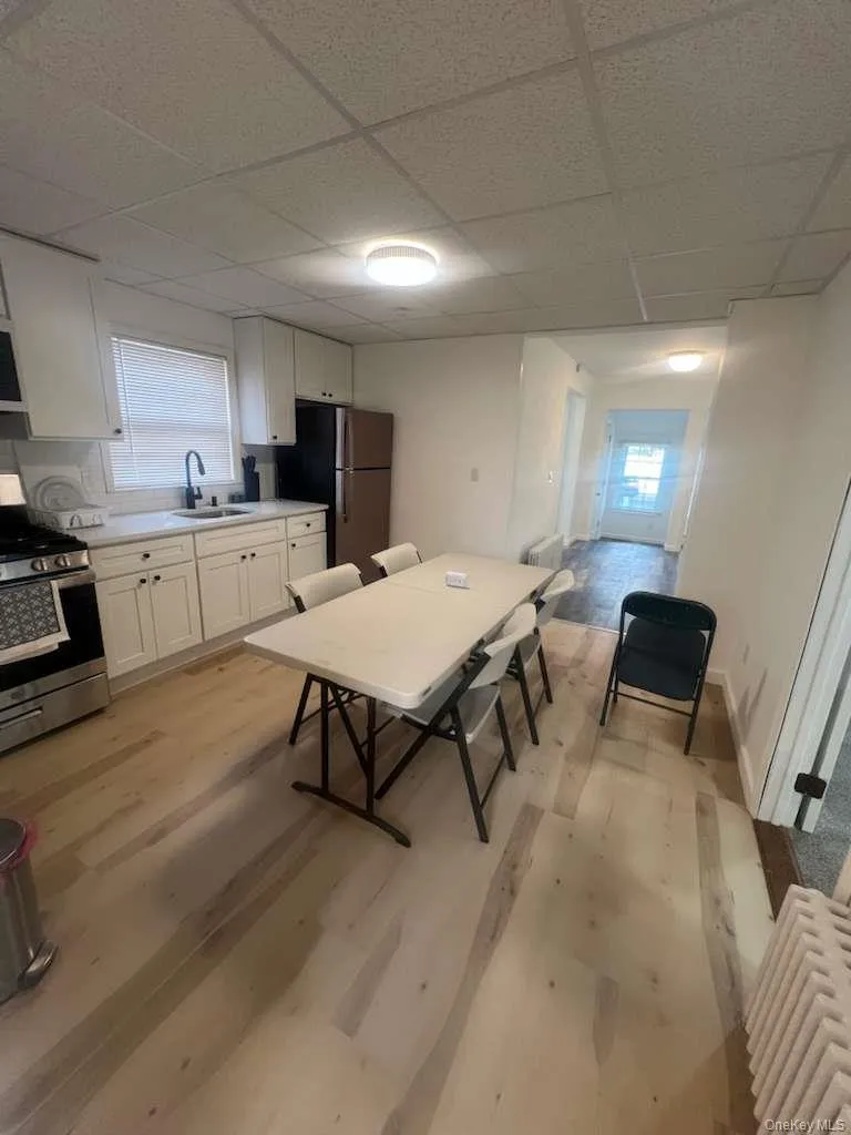 Kitchen featuring white cabinets, appliances with stainless steel finishes, plenty of natural light, light wood-style flooring, and a paneled ceiling Kitchen featuring white cabinets, appliances with stainless steel finishes, plenty of natural light, light wood-style flooring, and a paneled ceiling