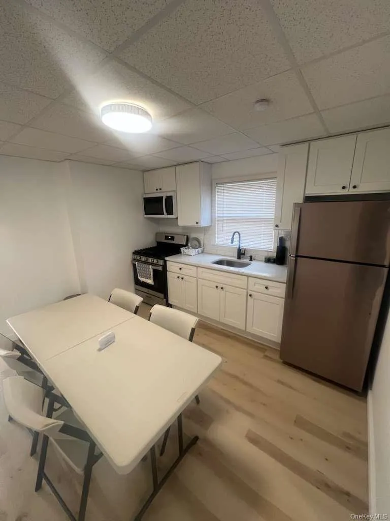 Kitchen with appliances with stainless steel finishes, white cabinets, light wood finished floors, a paneled ceiling, and light countertops Kitchen with appliances with stainless steel finishes, white cabinets, light wood finished floors, a paneled ceiling, and light countertops