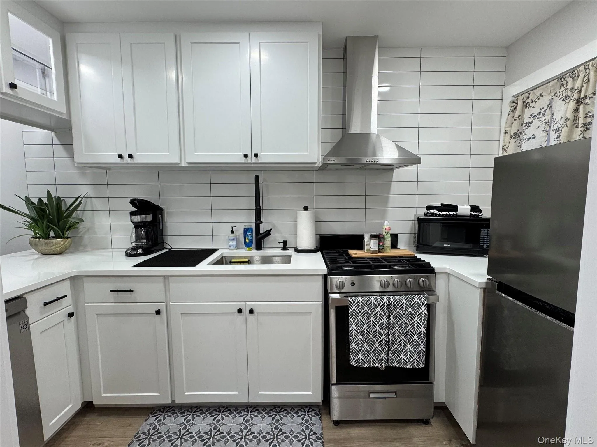Kitchen with stainless steel appliances, wall chimney range hood, white cabinetry, tasteful backsplash, and dark wood-style floors Kitchen with stainless steel appliances, wall chimney range hood, white cabinetry, tasteful backsplash, and dark wood-style floors