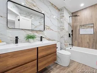 Bathroom featuring double vanity, tile walls, a combined bath / shower with marble appearance, and recessed lighting Bathroom featuring double vanity, tile walls, a combined bath / shower with marble appearance, and recessed lighting