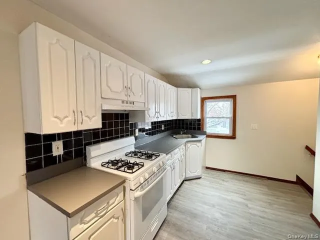 Kitchen with gas range gas stove, white cabinets, tasteful backsplash, light wood finished floors, and under cabinet range hood Kitchen with gas range gas stove, white cabinets, tasteful backsplash, light wood finished floors, and under cabinet range hood