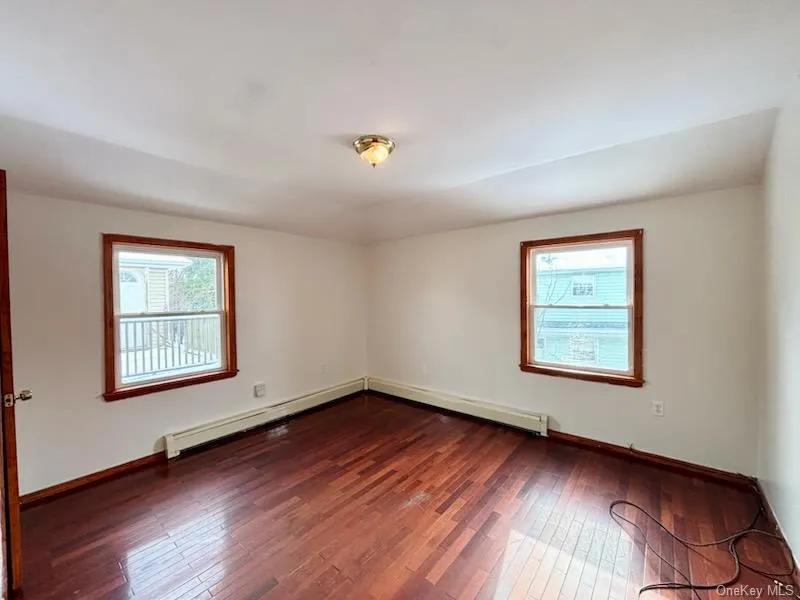 Spare room featuring dark wood-type flooring, healthy amount of natural light, and a baseboard radiator Spare room featuring dark wood-type flooring, healthy amount of natural light, and a baseboard radiator