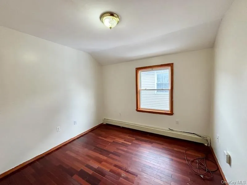 Unfurnished room with a baseboard heating unit, dark wood-style floors, and lofted ceiling Unfurnished room with a baseboard heating unit, dark wood-style floors, and lofted ceiling