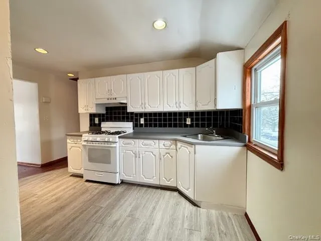 Kitchen with white range with gas stovetop, white cabinets, light wood-type flooring, tasteful backsplash, and recessed lighting Kitchen with white range with gas stovetop, white cabinets, light wood-type flooring, tasteful backsplash, and recessed lighting