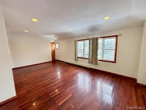 Empty room featuring dark wood finished floors, lofted ceiling, a baseboard heating unit, and recessed lighting Empty room featuring dark wood finished floors, lofted ceiling, a baseboard heating unit, and recessed lighting