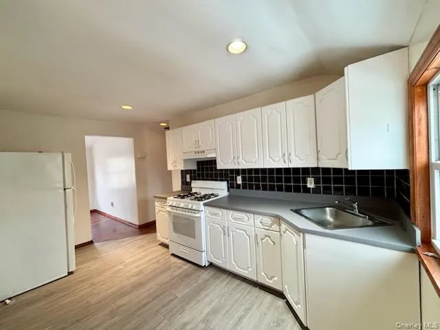 Kitchen with white appliances, white cabinets, light wood-type flooring, tasteful backsplash, and recessed lighting Kitchen with white appliances, white cabinets, light wood-type flooring, tasteful backsplash, and recessed lighting