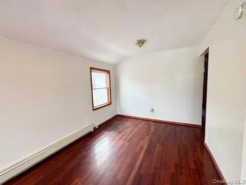 Unfurnished room with a baseboard radiator, dark wood-style flooring, lofted ceiling, and a smoke detector Unfurnished room with a baseboard radiator, dark wood-style flooring, lofted ceiling, and a smoke detector