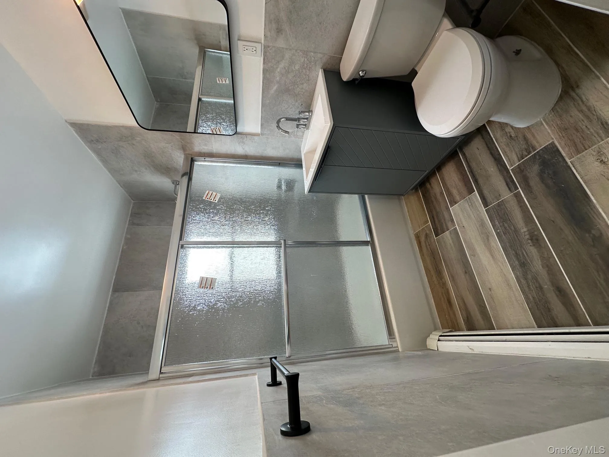 Bathroom featuring shower / bath combination with glass door, tile walls, vanity, wood tiled floors, and baseboard heating Bathroom featuring shower / bath combination with glass door, tile walls, vanity, wood tiled floors, and baseboard heating