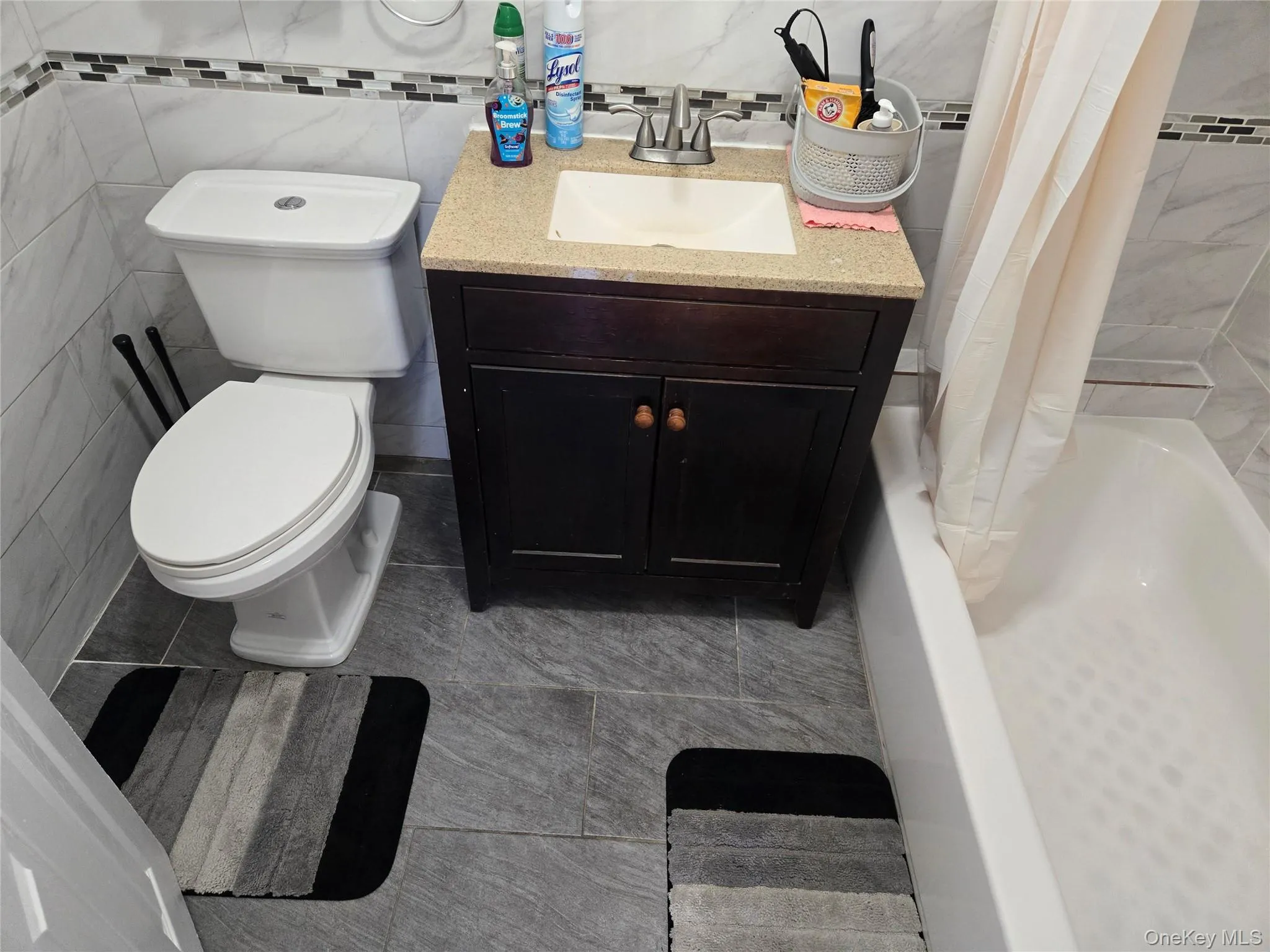 Bathroom with tile walls, vanity, shower / bath combo and light tile patterned floors Bathroom with tile walls, vanity, shower / bath combo and light tile patterned floors