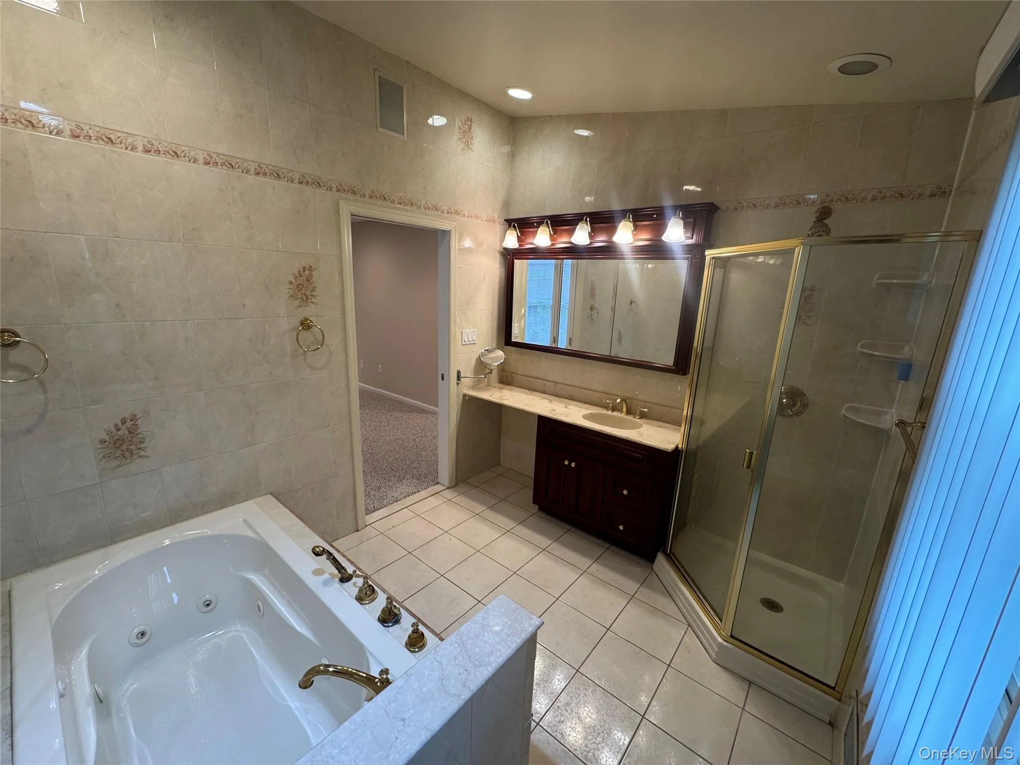 Full bathroom with vanity, light tile patterned flooring, a tub with jets, tile walls, and a stall shower Full bathroom with vanity, light tile patterned flooring, a tub with jets, tile walls, and a stall shower