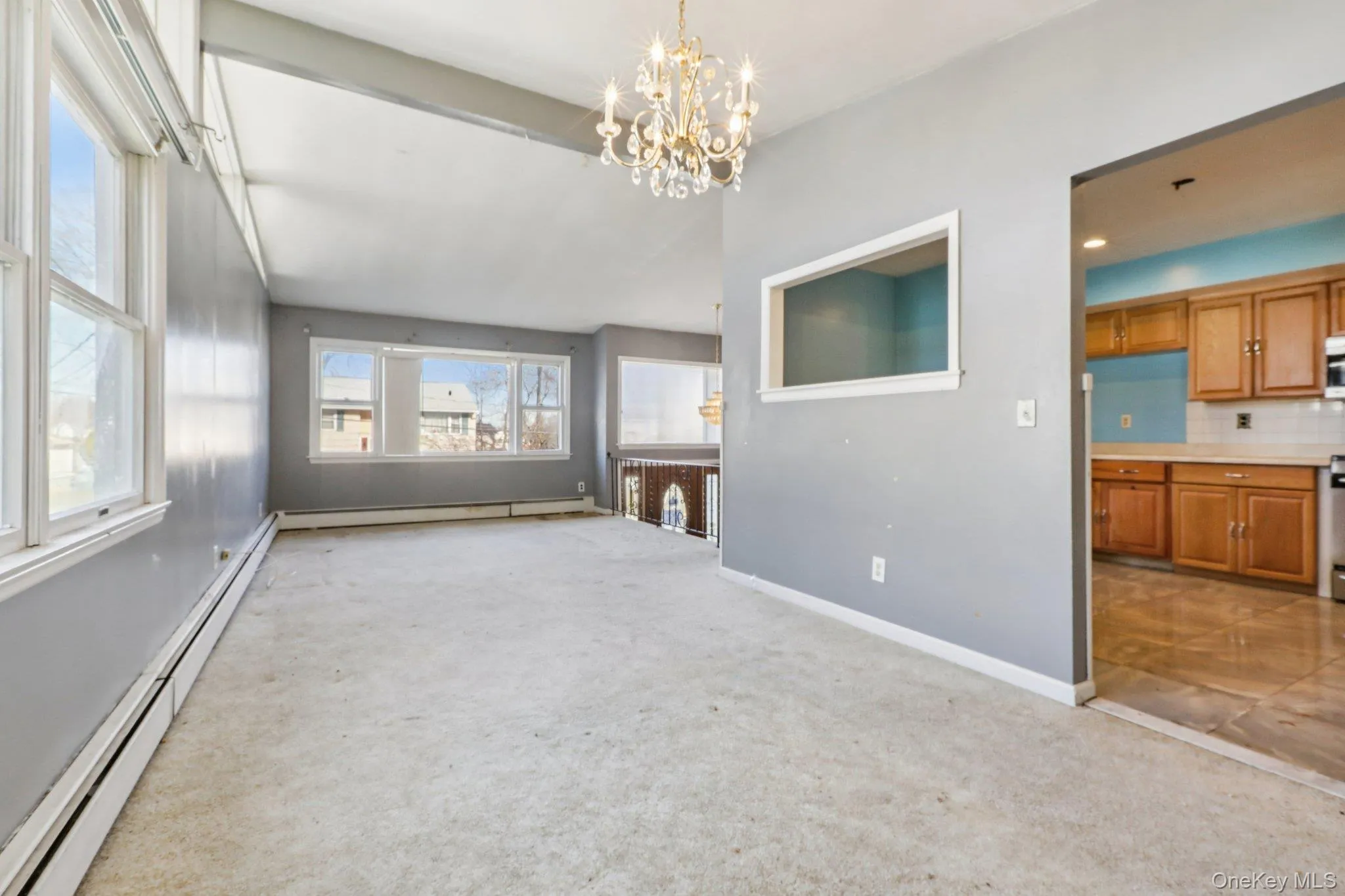 Unfurnished living room with a baseboard radiator, a chandelier, and light carpet Unfurnished living room with a baseboard radiator, a chandelier, and light carpet