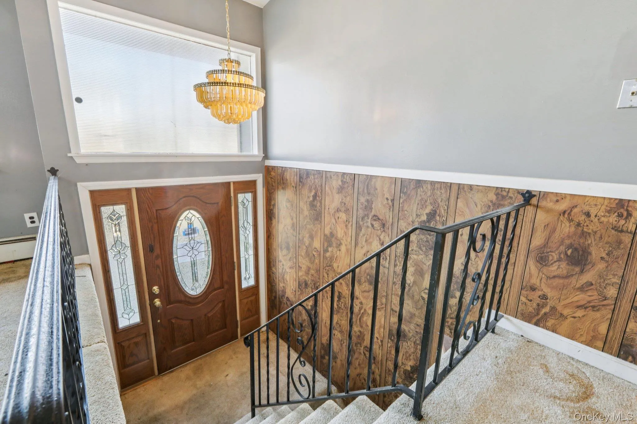 Carpeted foyer entrance with stairs, a chandelier, wood walls, and wainscoting Carpeted foyer entrance with stairs, a chandelier, wood walls, and wainscoting