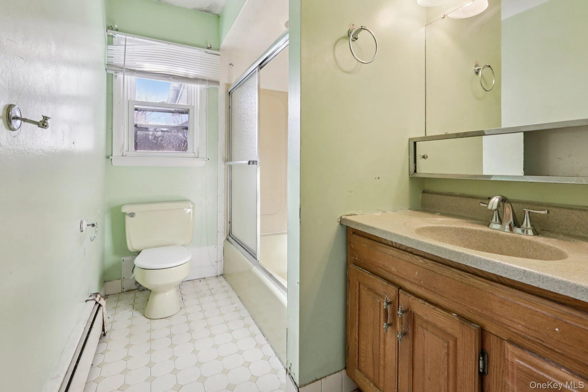 Full bath with a baseboard heating unit, vanity, combined bath / shower with glass door, and light flooring Full bath with a baseboard heating unit, vanity, combined bath / shower with glass door, and light flooring