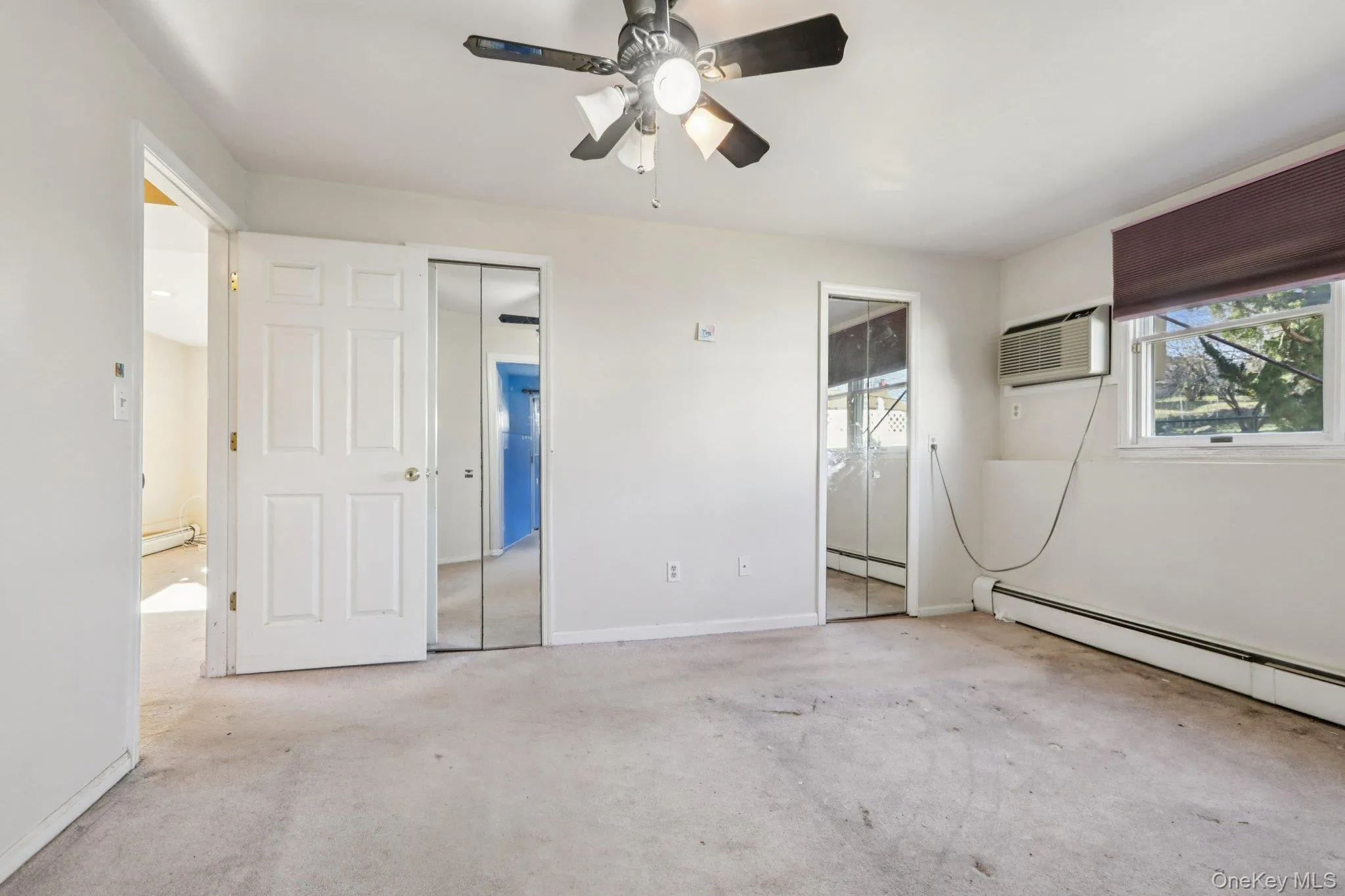 Unfurnished bedroom with light colored carpet, ceiling fan, a closet, a baseboard heating unit, and a wall mounted AC Unfurnished bedroom with light colored carpet, ceiling fan, a closet, a baseboard heating unit, and a wall mounted AC
