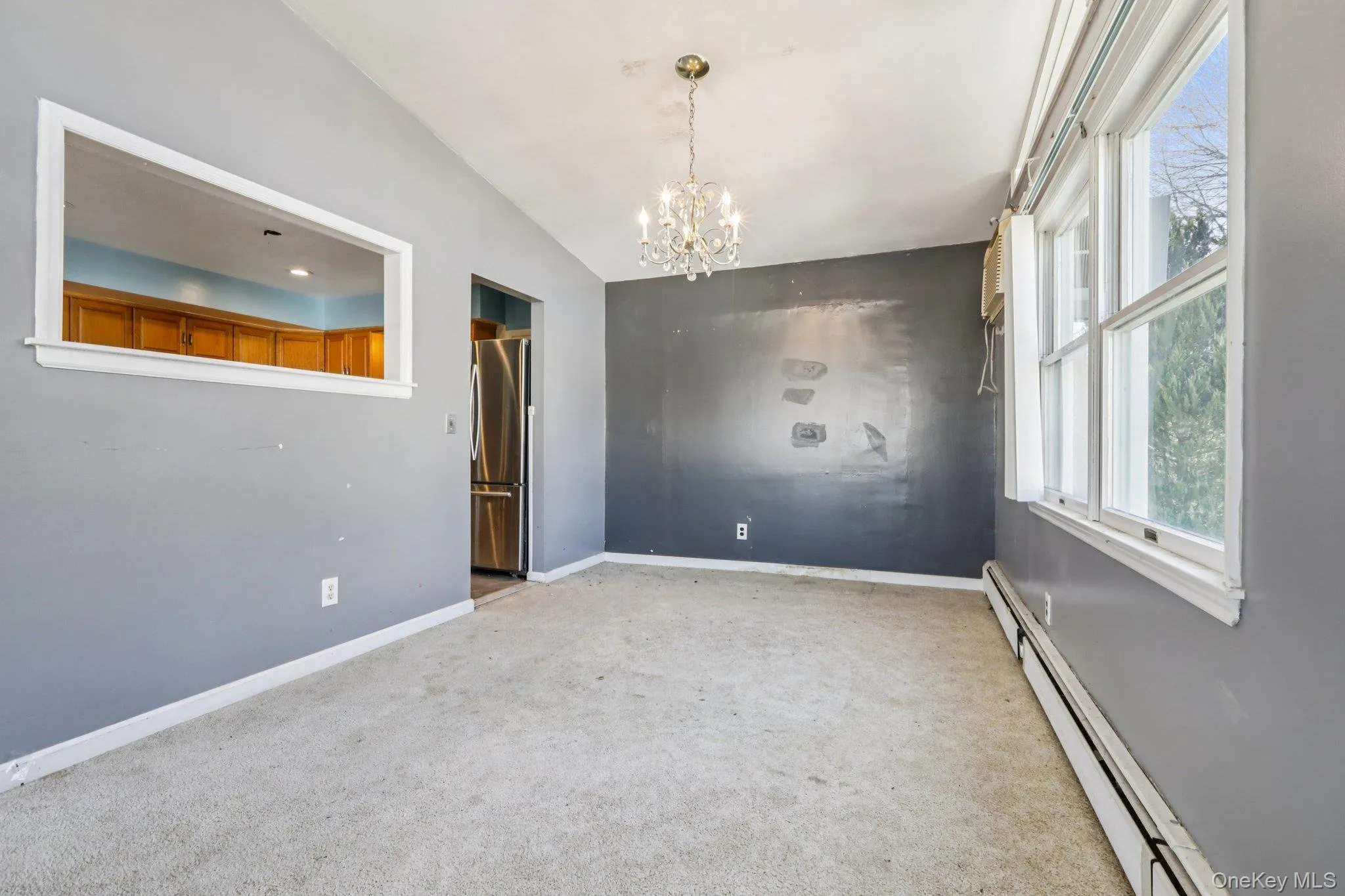 Empty room featuring a baseboard heating unit, vaulted ceiling, a chandelier, and light colored carpet Empty room featuring a baseboard heating unit, vaulted ceiling, a chandelier, and light colored carpet