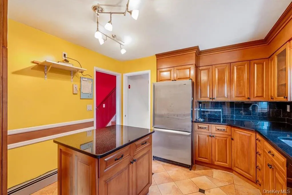 Kitchen with brown cabinets, freestanding refrigerator, dark stone countertops, tasteful backsplash, and a baseboard heating unit Kitchen with brown cabinets, freestanding refrigerator, dark stone countertops, tasteful backsplash, and a baseboard heating unit