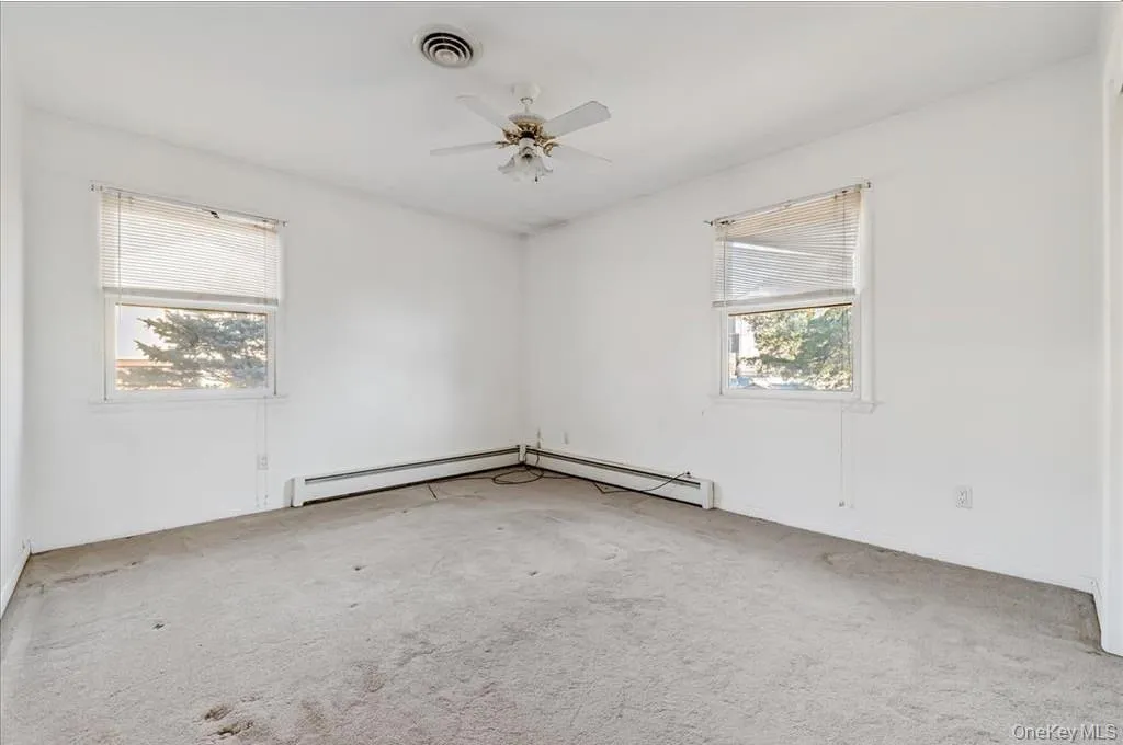 Unfurnished room featuring light carpet, baseboard heating, and ceiling fan Unfurnished room featuring light carpet, baseboard heating, and ceiling fan