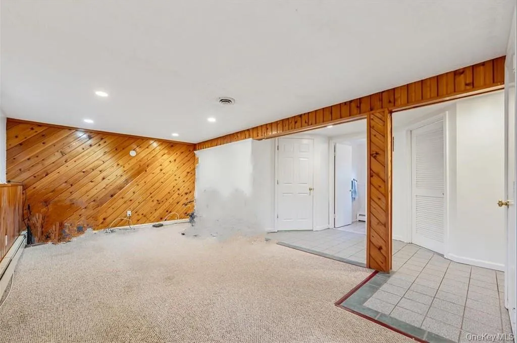 Below grade area featuring wood walls, carpet, a baseboard radiator, and recessed lighting Below grade area featuring wood walls, carpet, a baseboard radiator, and recessed lighting