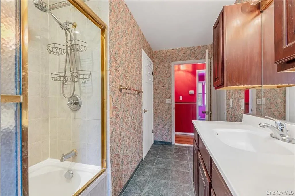 Full bath featuring wallpapered walls, vanity, and enclosed tub / shower combo Full bath featuring wallpapered walls, vanity, and enclosed tub / shower combo