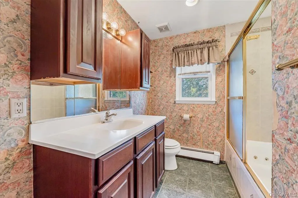 Full bath with wallpapered walls, vanity, a baseboard heating unit, and a combined bath / shower with jetted tub Full bath with wallpapered walls, vanity, a baseboard heating unit, and a combined bath / shower with jetted tub