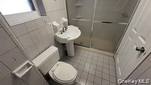 Bathroom featuring tile walls, a shower stall, and light tile patterned floors Bathroom featuring tile walls, a shower stall, and light tile patterned floors