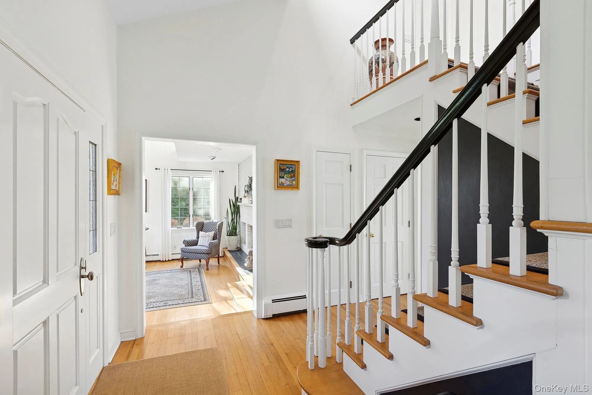 Foyer with light wood-style floors, a towering ceiling, a baseboard radiator, and stairway Foyer with light wood-style floors, a towering ceiling, a baseboard radiator, and stairway