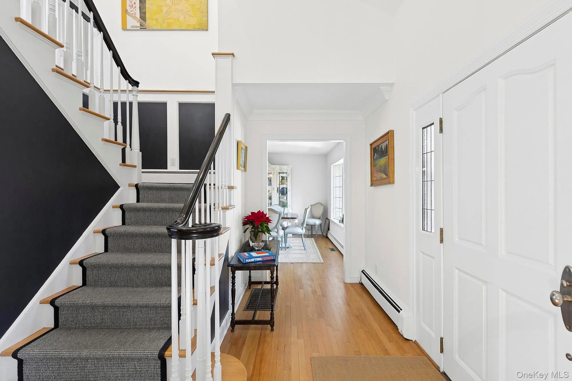 Foyer entrance featuring baseboard heating, light wood finished floors, ornamental molding, and stairway Foyer entrance featuring baseboard heating, light wood finished floors, ornamental molding, and stairway