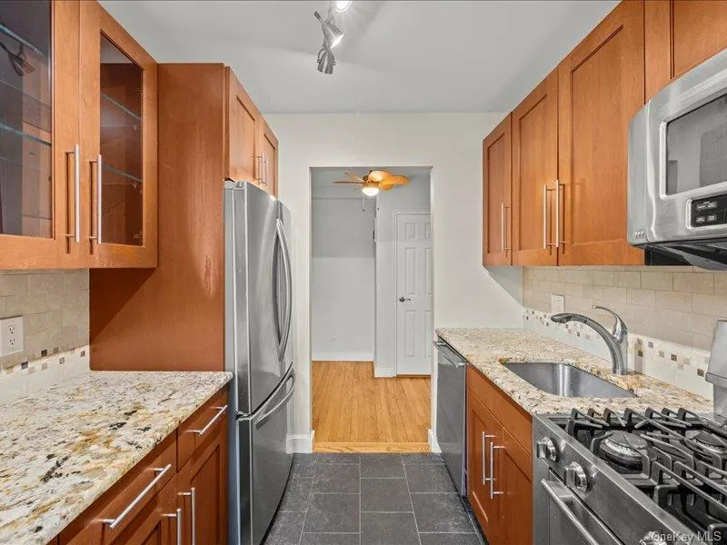 Kitchen with tasteful backsplash, stainless steel appliances, light stone counters, glass insert cabinets, and brown cabinets Kitchen with tasteful backsplash, stainless steel appliances, light stone counters, glass insert cabinets, and brown cabinets