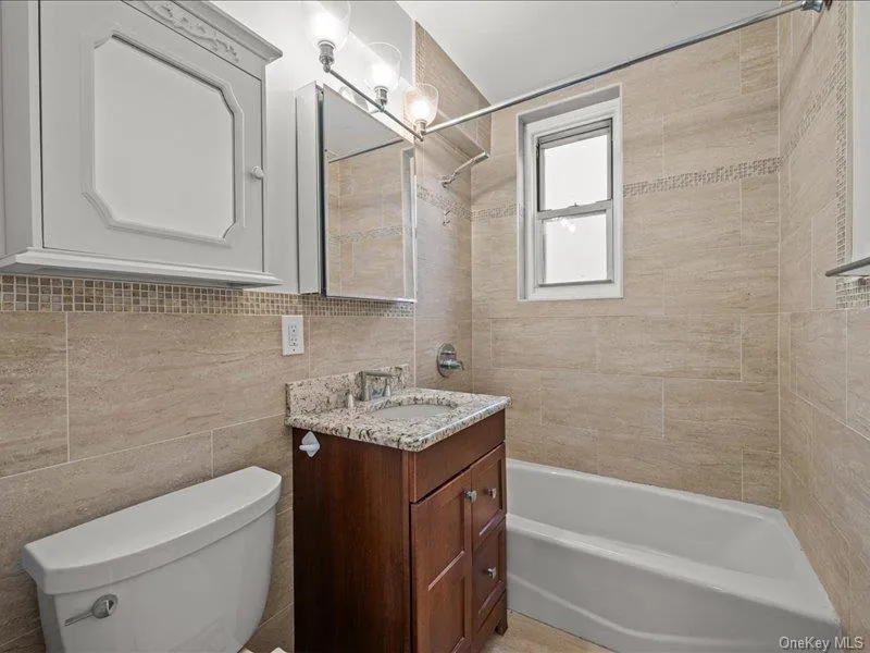 Full bathroom with bathtub / shower combination, vanity, and tile walls Full bathroom with bathtub / shower combination, vanity, and tile walls