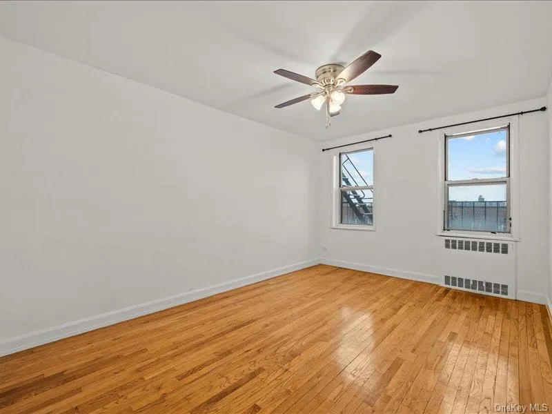 Unfurnished room featuring radiator heating unit, light wood-type flooring, and a ceiling fan Unfurnished room featuring radiator heating unit, light wood-type flooring, and a ceiling fan