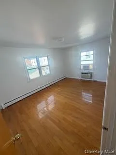 Unfurnished room with a baseboard heating unit, plenty of natural light, and wood finished floors Unfurnished room with a baseboard heating unit, plenty of natural light, and wood finished floors