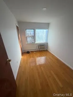 Unfurnished room with wood finished floors and a baseboard heating unit Unfurnished room with wood finished floors and a baseboard heating unit