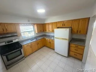 Kitchen featuring stainless steel stove, freestanding refrigerator, and brown cabinets Kitchen featuring stainless steel stove, freestanding refrigerator, and brown cabinets