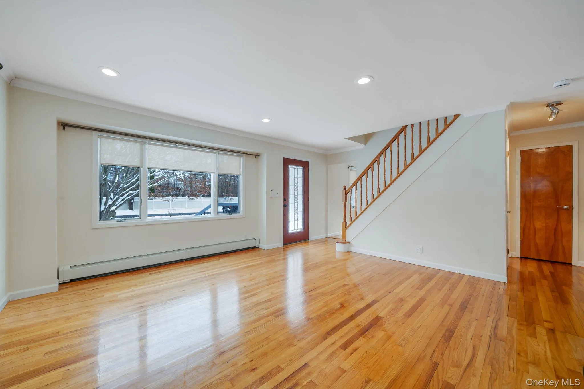 Living room with crown molding, ductless AC, stairway, a baseboard radiator, hardwood floors, and recessed lighting. Living room with crown molding, ductless AC, stairway, a baseboard radiator, hardwood floors, and recessed lighting.