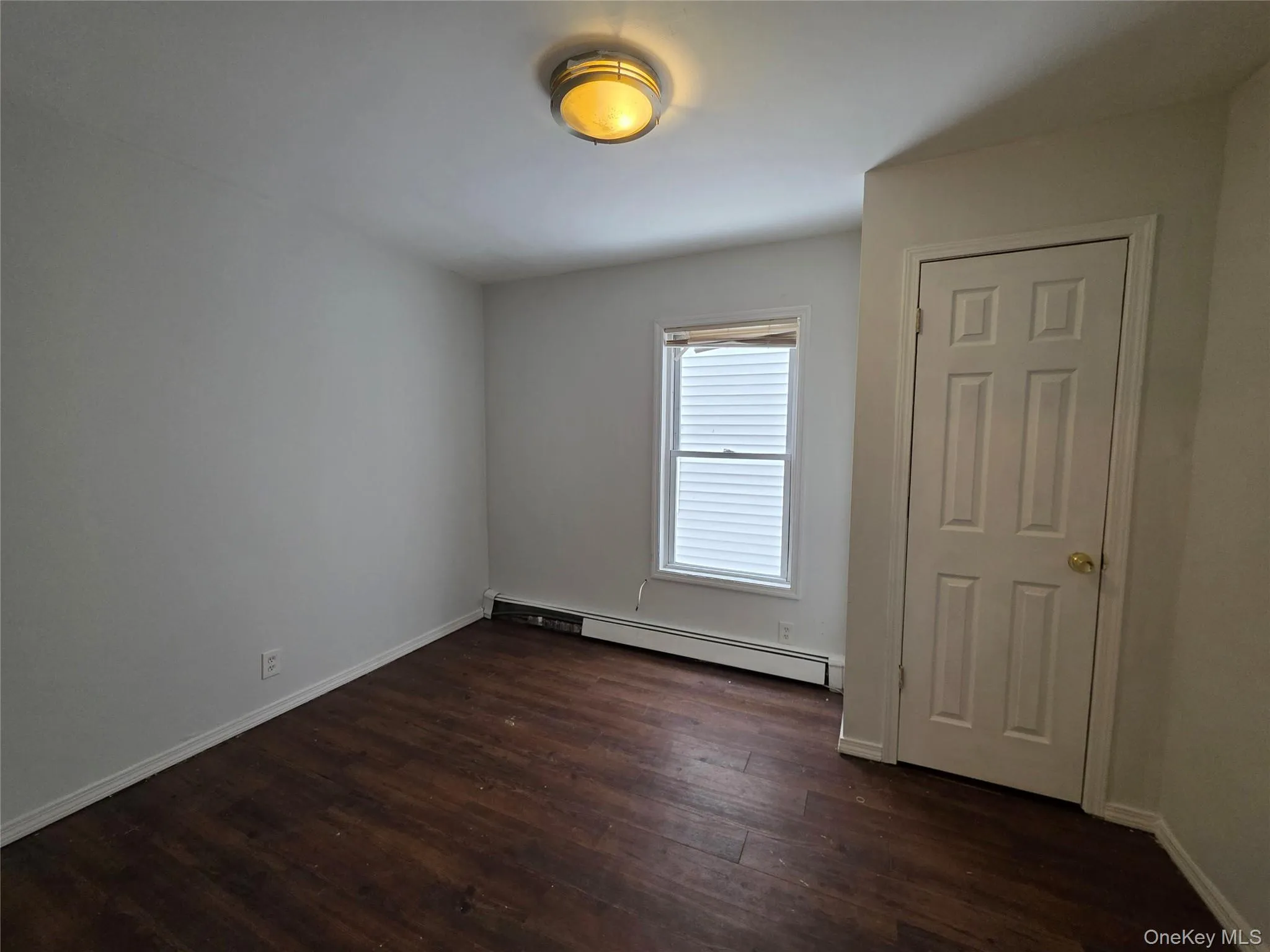 Unfurnished room featuring a baseboard heating unit and dark wood-style floors Unfurnished room featuring a baseboard heating unit and dark wood-style floors