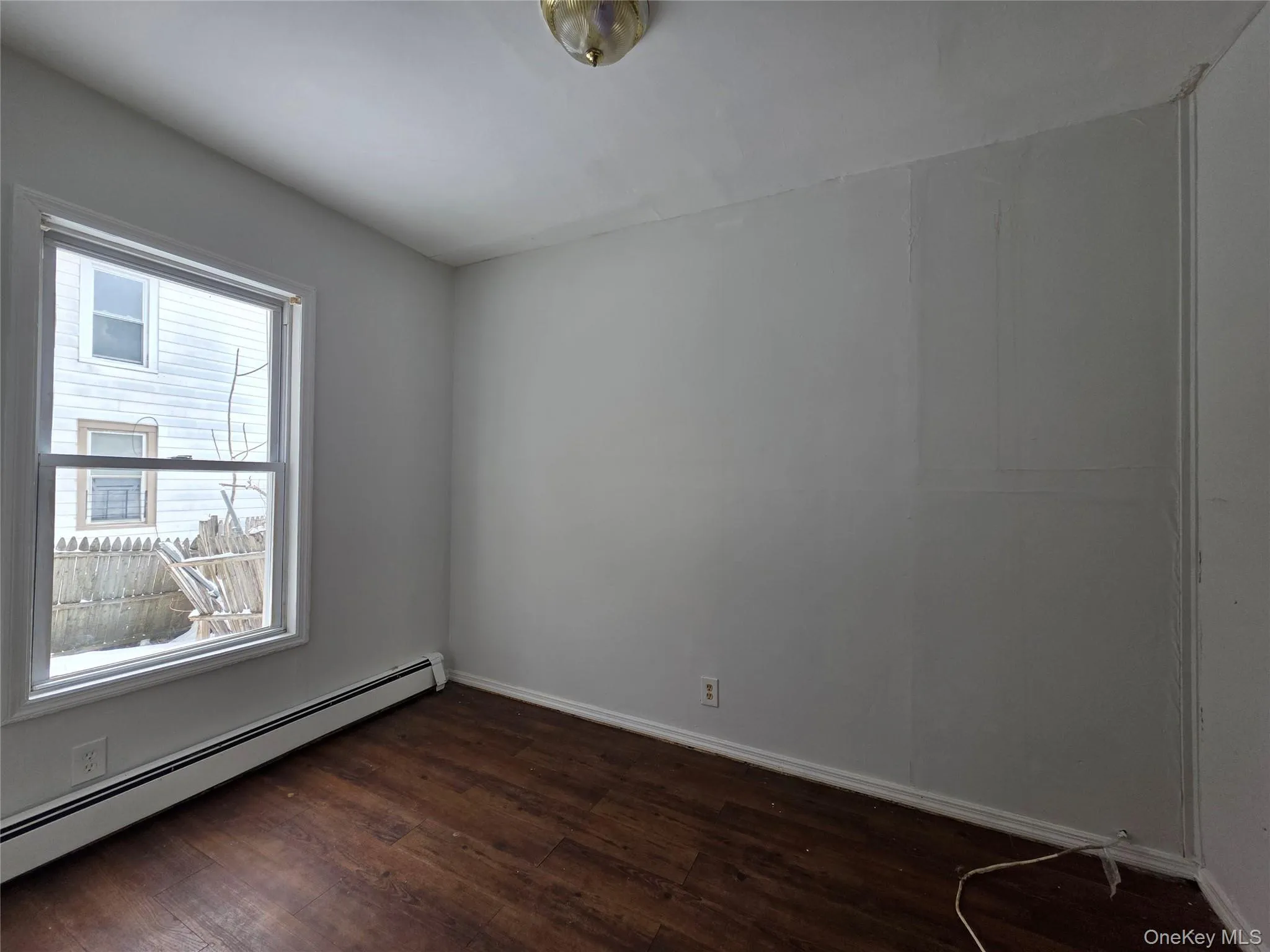 Empty room with baseboard heating and dark wood finished floors Empty room with baseboard heating and dark wood finished floors