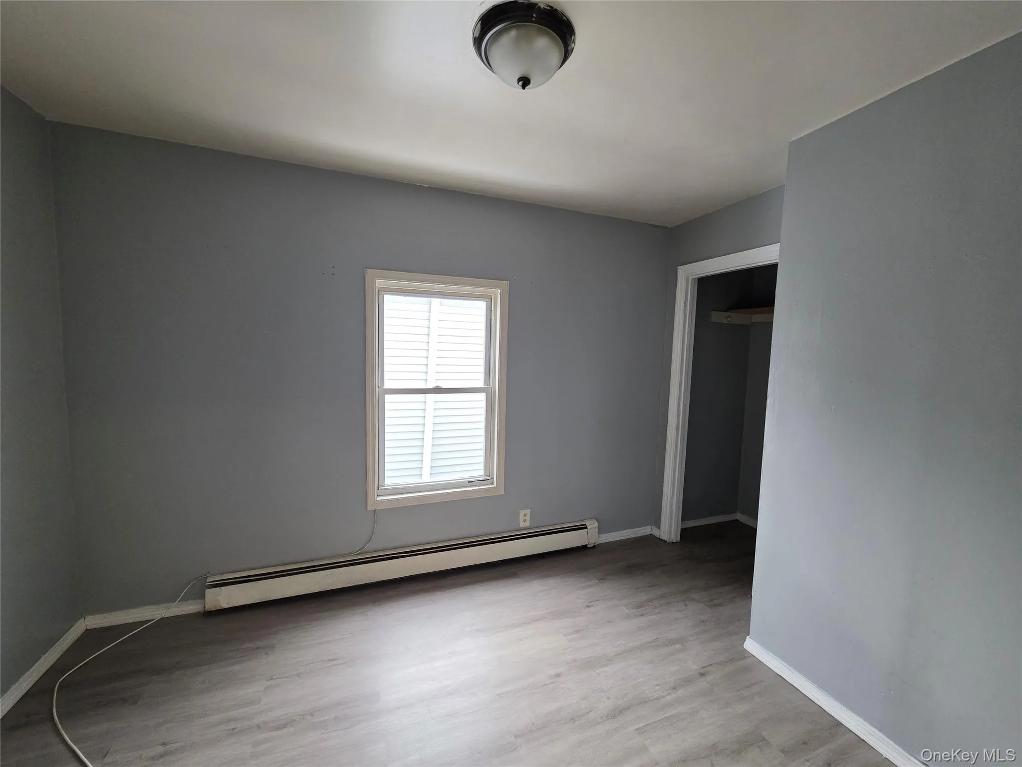 Unfurnished bedroom featuring a baseboard heating unit, light wood-style flooring, and a closet Unfurnished bedroom featuring a baseboard heating unit, light wood-style flooring, and a closet