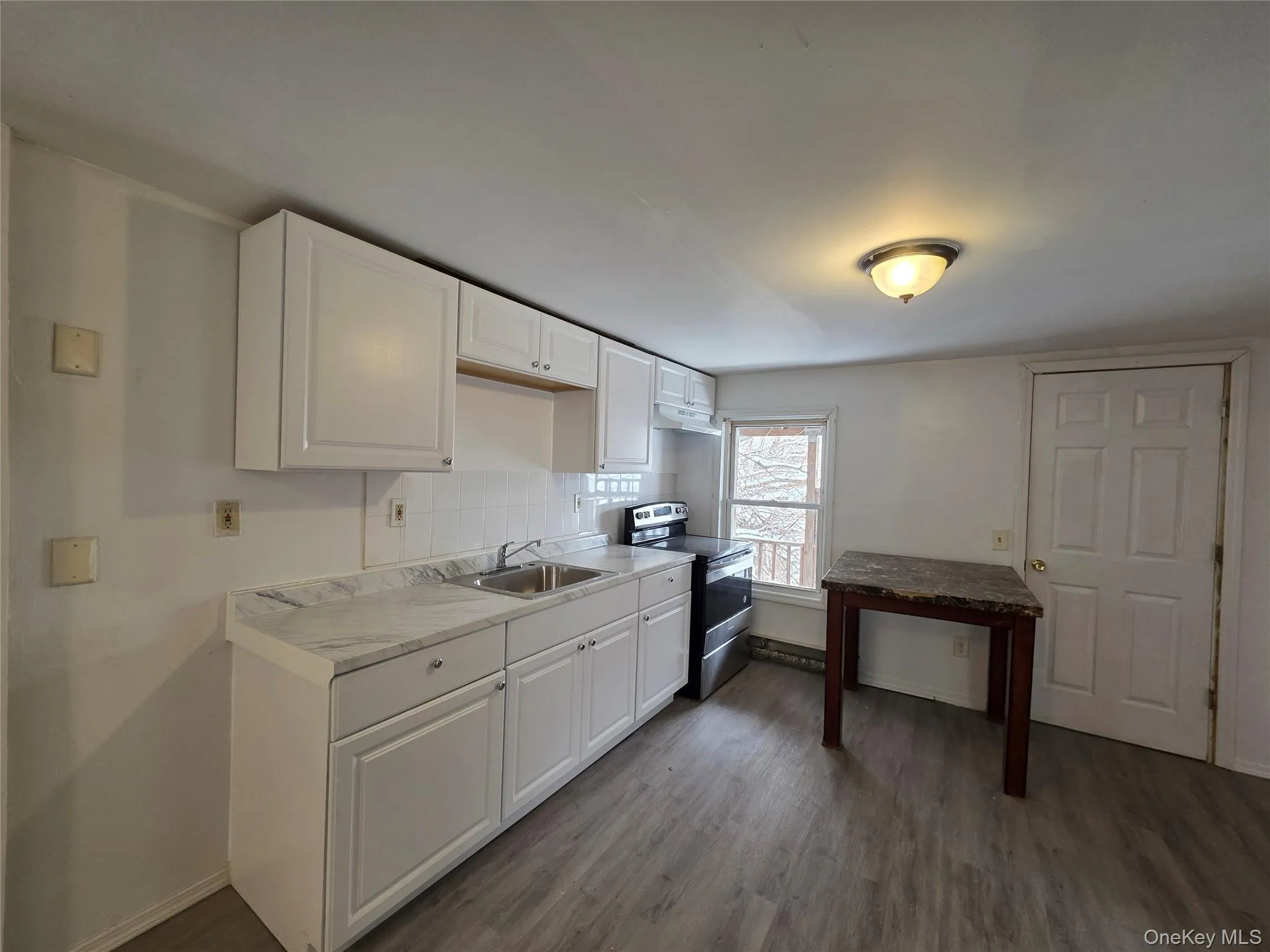 Kitchen with white cabinetry, stainless steel electric range, light countertops, decorative backsplash, and dark wood-type flooring Kitchen with white cabinetry, stainless steel electric range, light countertops, decorative backsplash, and dark wood-type flooring