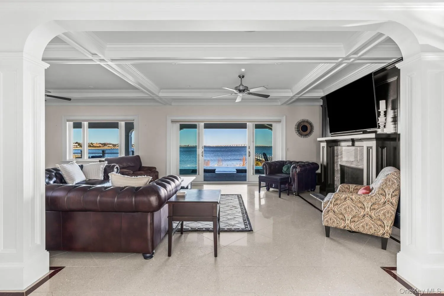 Living room featuring arched walkways, a high end fireplace, ceiling fan, coffered ceiling, and ornate columns Living room featuring arched walkways, a high end fireplace, ceiling fan, coffered ceiling, and ornate columns