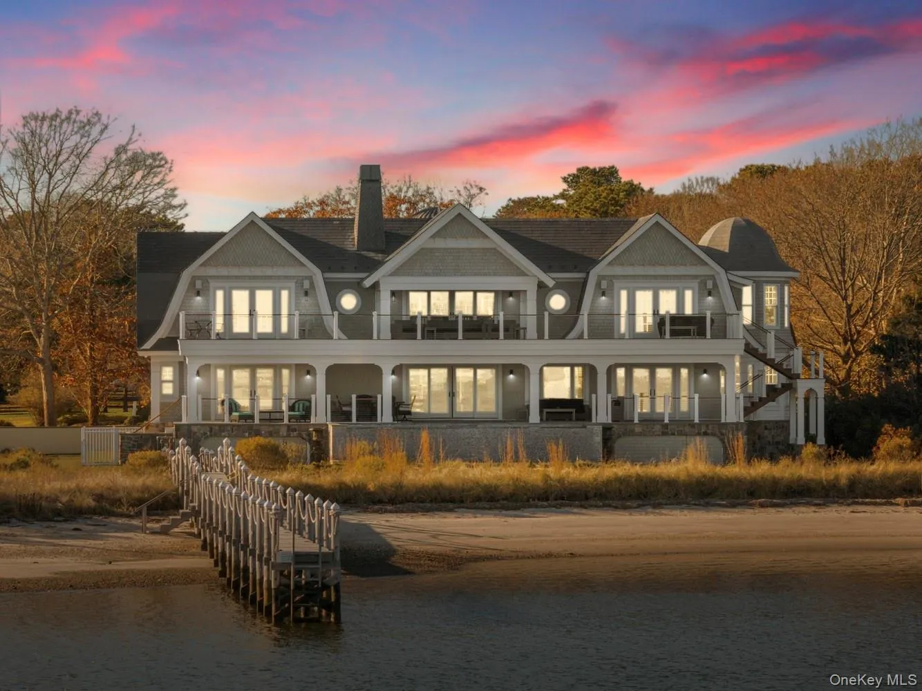 Back of house at dusk featuring a gambrel roof, a chimney, stairs, and covered porch Back of house at dusk featuring a gambrel roof, a chimney, stairs, and covered porch