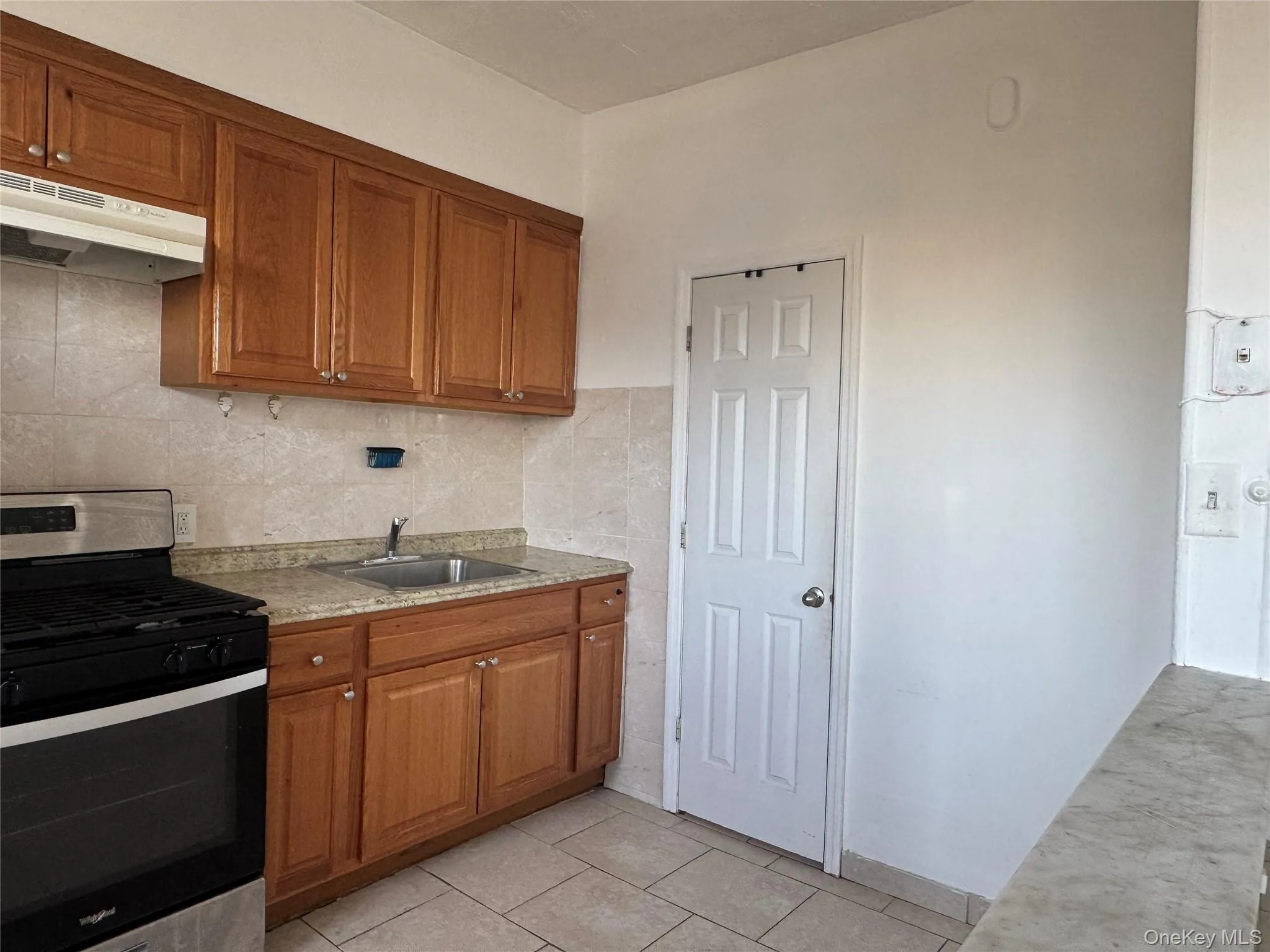 Kitchen with stainless steel gas range oven, brown cabinets, under cabinet range hood, light tile patterned flooring, and decorative backsplash Kitchen with stainless steel gas range oven, brown cabinets, under cabinet range hood, light tile patterned flooring, and decorative backsplash