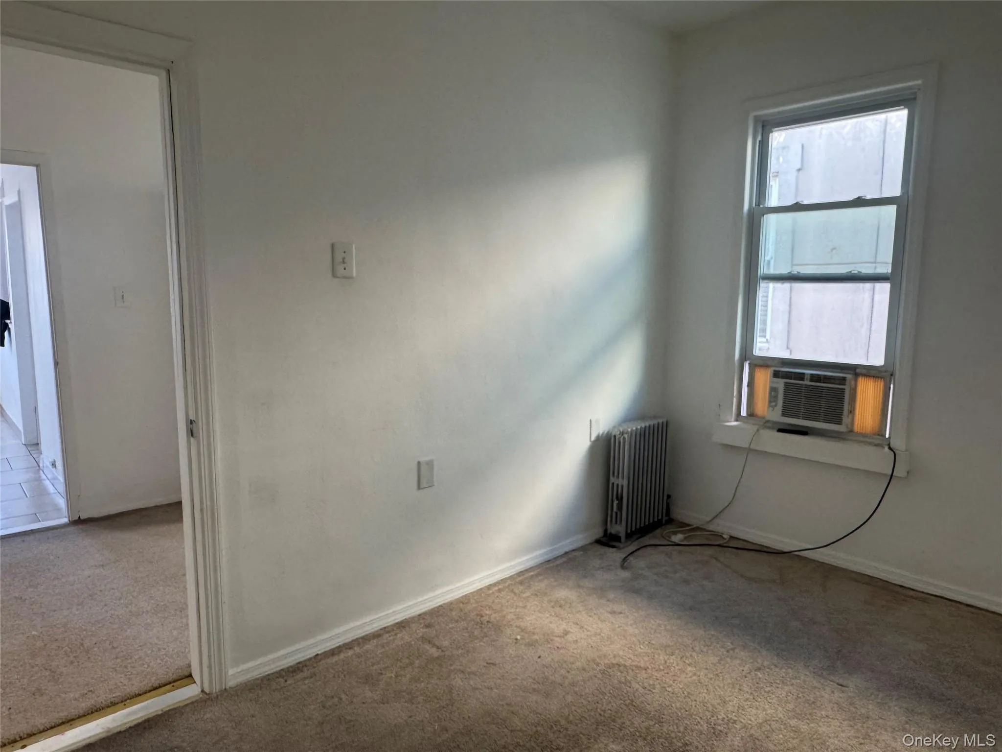 Empty room with carpet floors, radiator heating unit, and cooling unit Empty room with carpet floors, radiator heating unit, and cooling unit