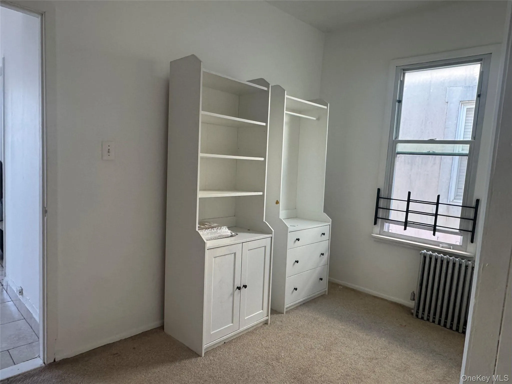 Unfurnished bedroom featuring radiator and light carpet Unfurnished bedroom featuring radiator and light carpet
