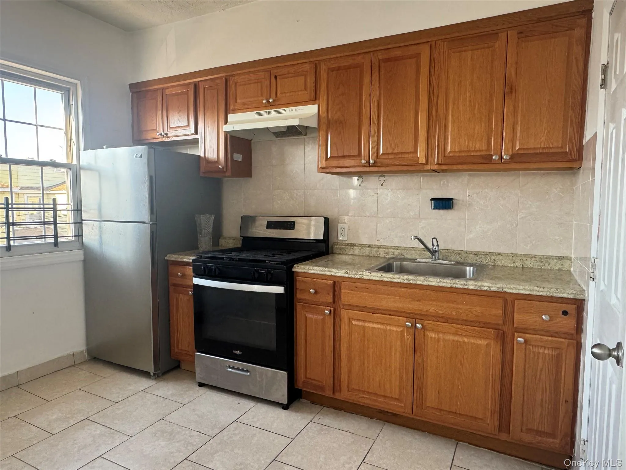 Kitchen with brown cabinets, stainless steel appliances, under cabinet range hood, and backsplash Kitchen with brown cabinets, stainless steel appliances, under cabinet range hood, and backsplash