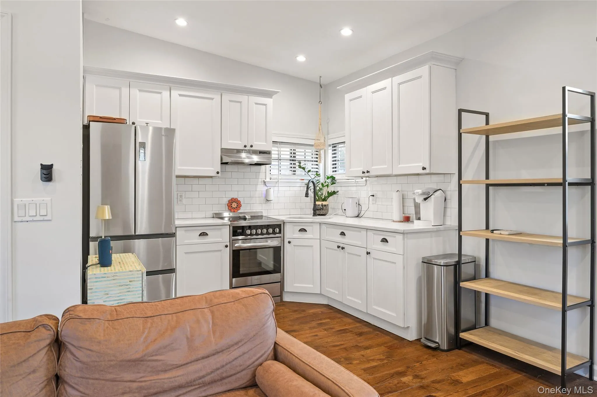 Kitchen with white cabinets, appliances with stainless steel finishes, dark wood-style flooring, vaulted ceiling, and decorative backsplash Kitchen with white cabinets, appliances with stainless steel finishes, dark wood-style flooring, vaulted ceiling, and decorative backsplash