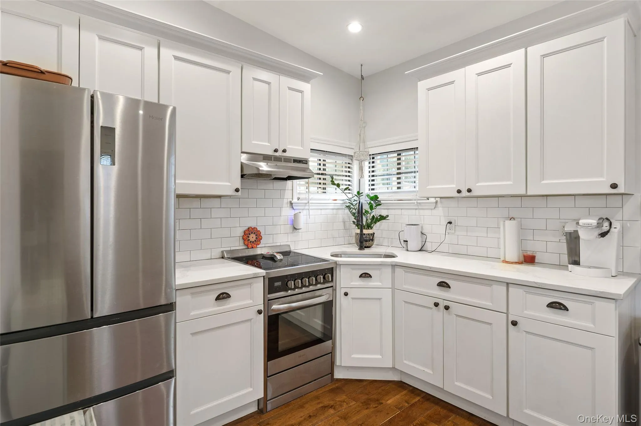 Kitchen featuring stainless steel appliances, white cabinets, under cabinet range hood, dark wood-style flooring, and light stone counters Kitchen featuring stainless steel appliances, white cabinets, under cabinet range hood, dark wood-style flooring, and light stone counters