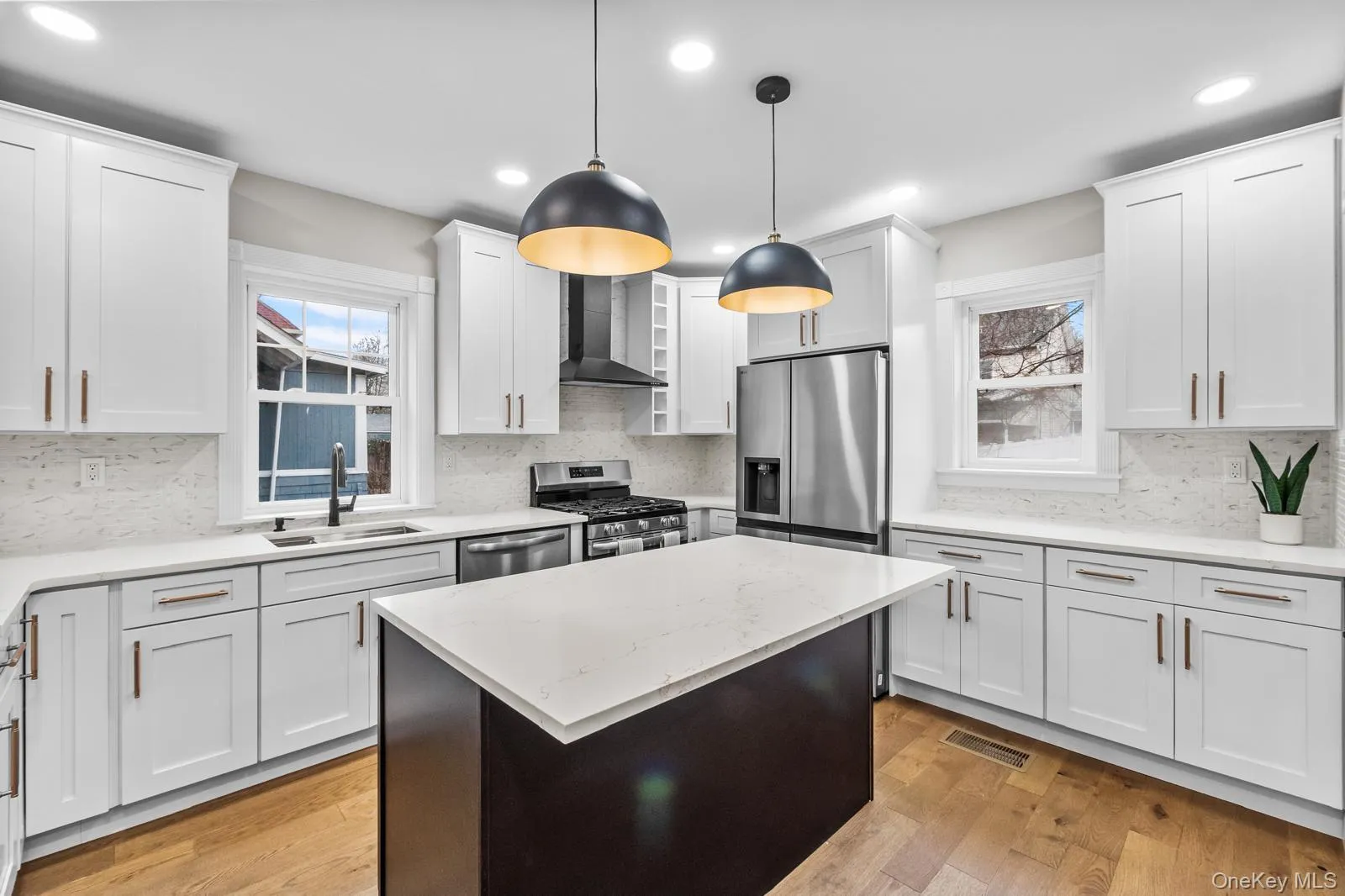 Kitchen with stainless steel appliances, light stone countertops, decorative light fixtures, a kitchen island, and wall chimney exhaust hood Kitchen with stainless steel appliances, light stone countertops, decorative light fixtures, a kitchen island, and wall chimney exhaust hood