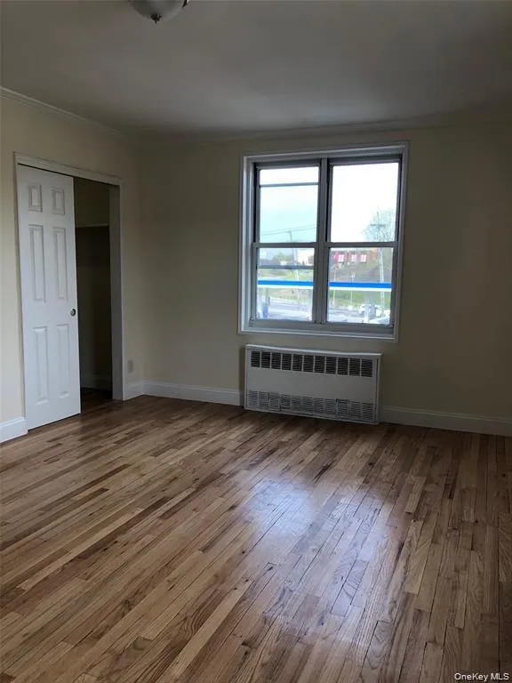 Empty room with radiator heating unit, ornamental molding, and wood-type flooring Empty room with radiator heating unit, ornamental molding, and wood-type flooring